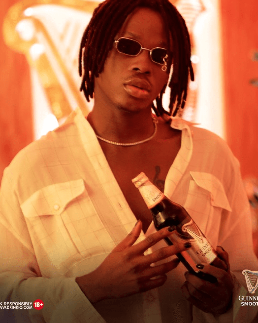 Fireboy DML with glasses on holding a bottle of guiness